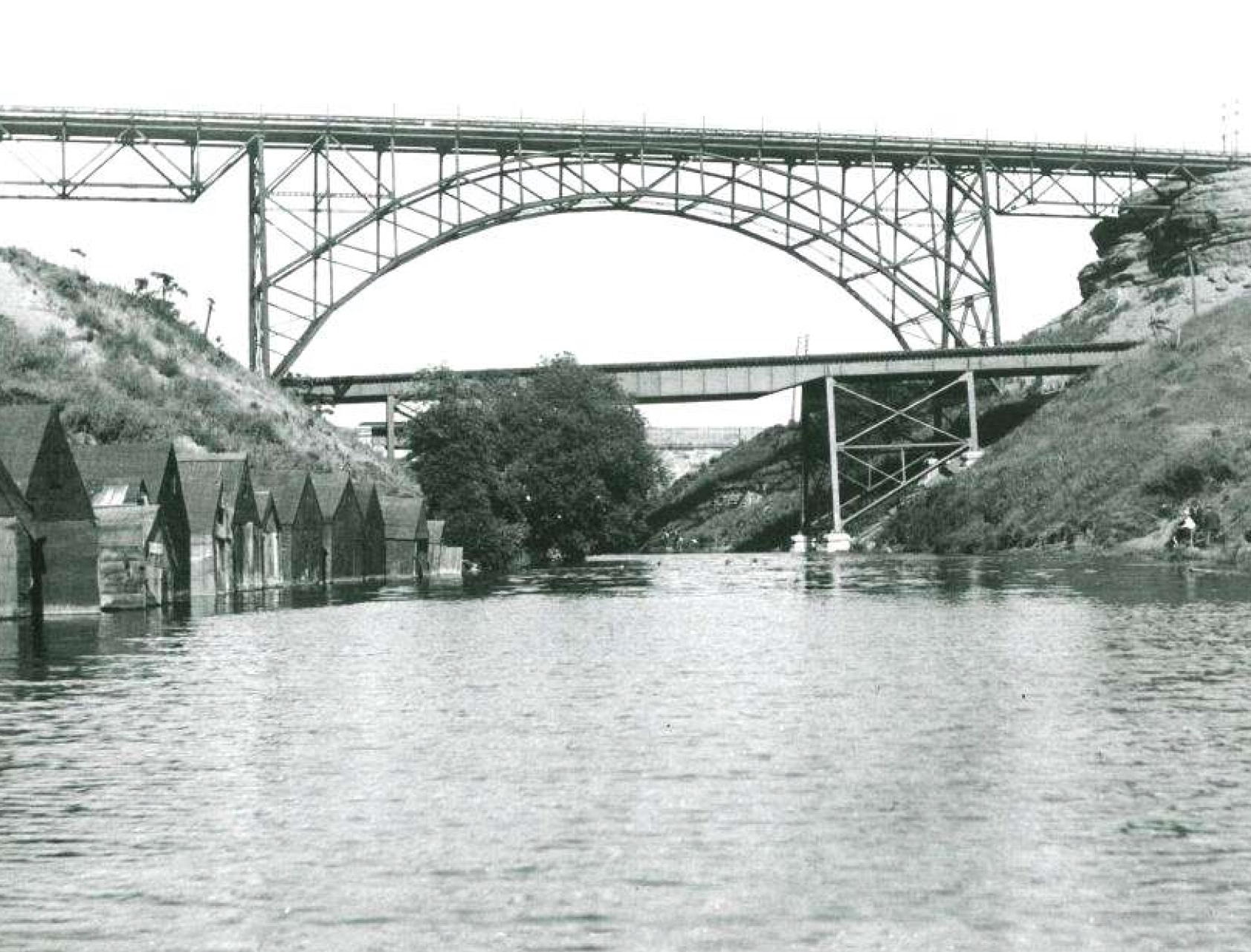 Historical photo of the Canal from Cootes Paradise to Hamilton Harbour in 1928, with pedestrian and rail bridges overtop and fishing huts along the shore