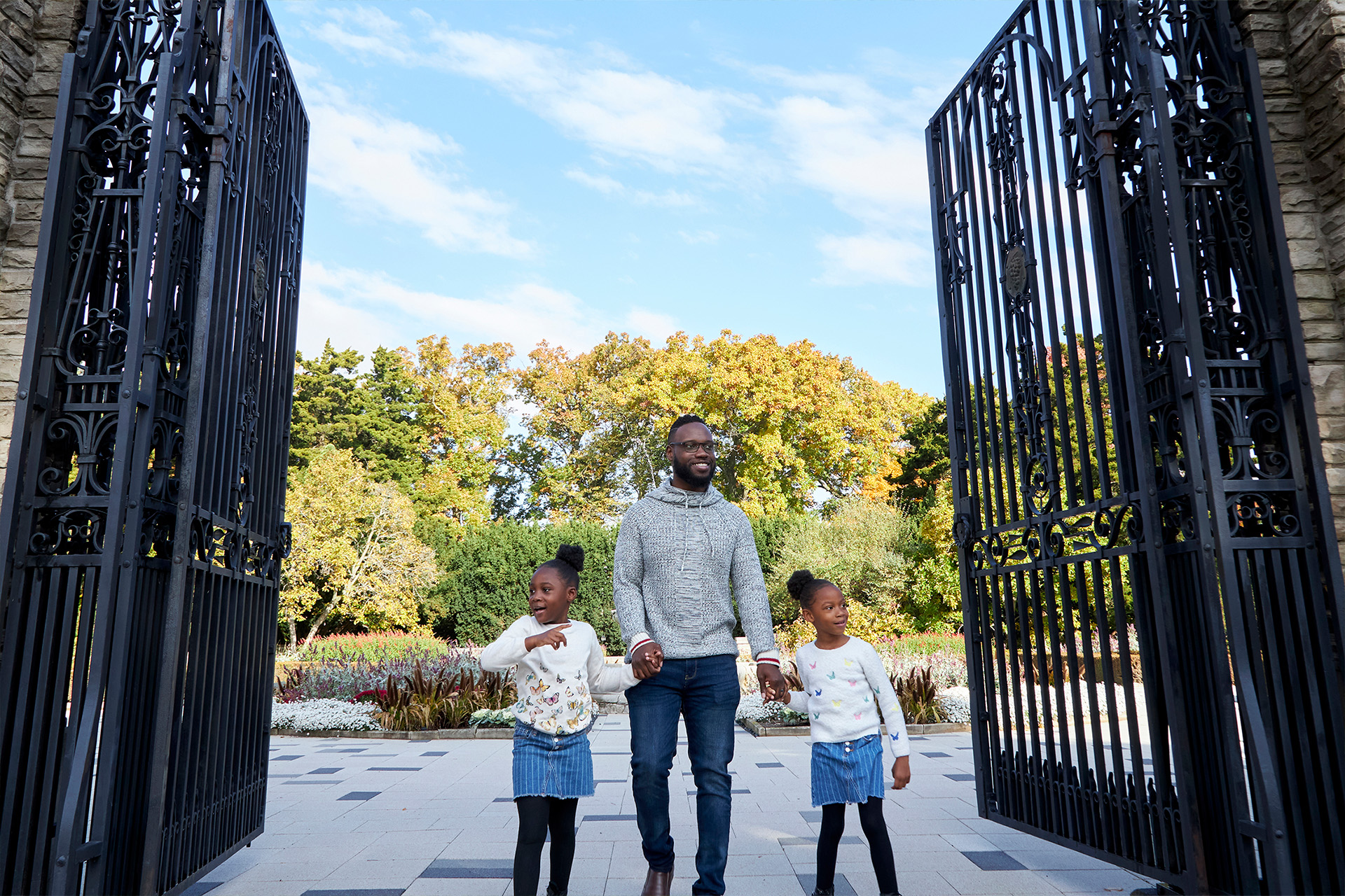 Father and daughters walking through large metal gates in hendrie park