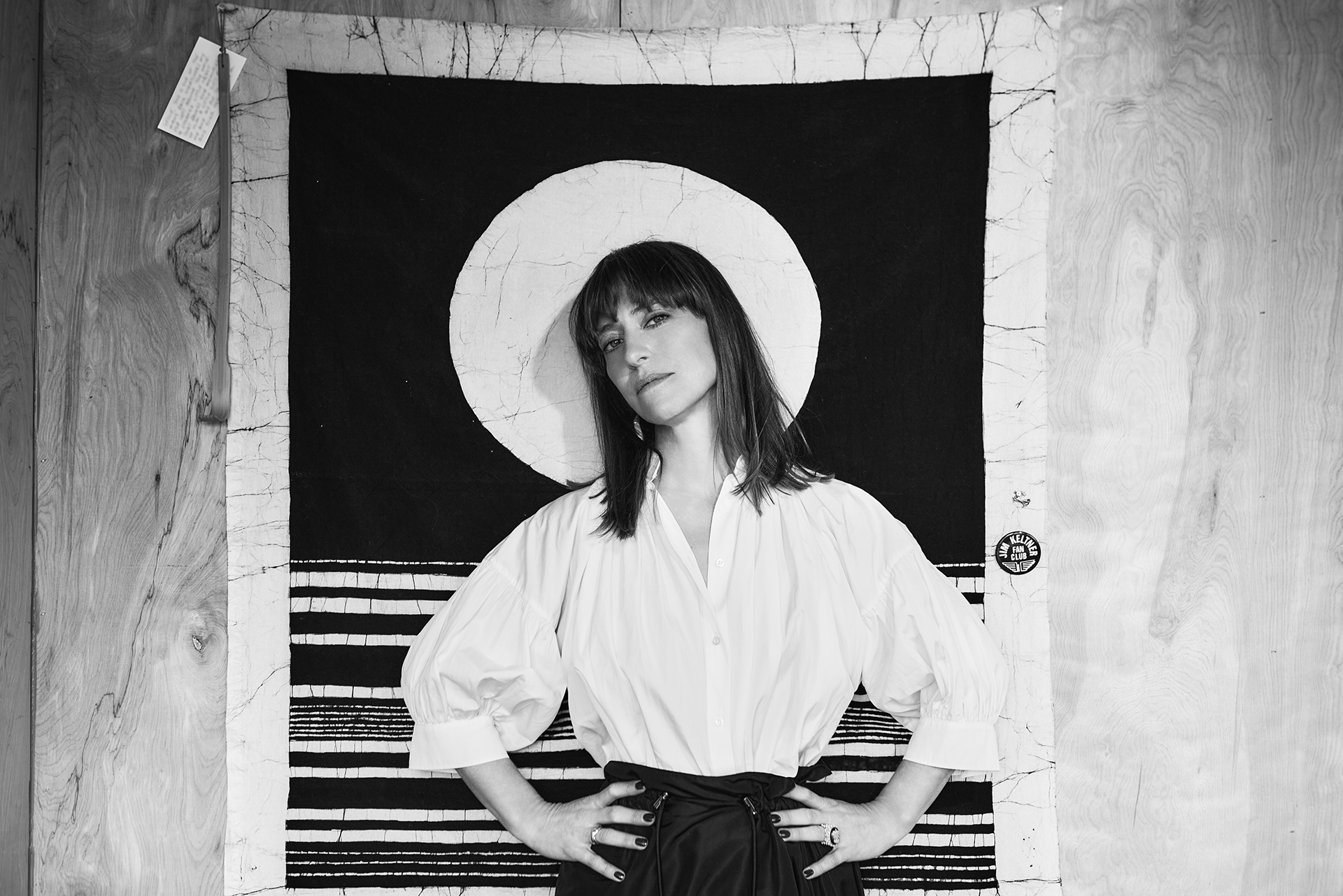 A black and white photo of Feist standing in front of a piece of abstract artwork