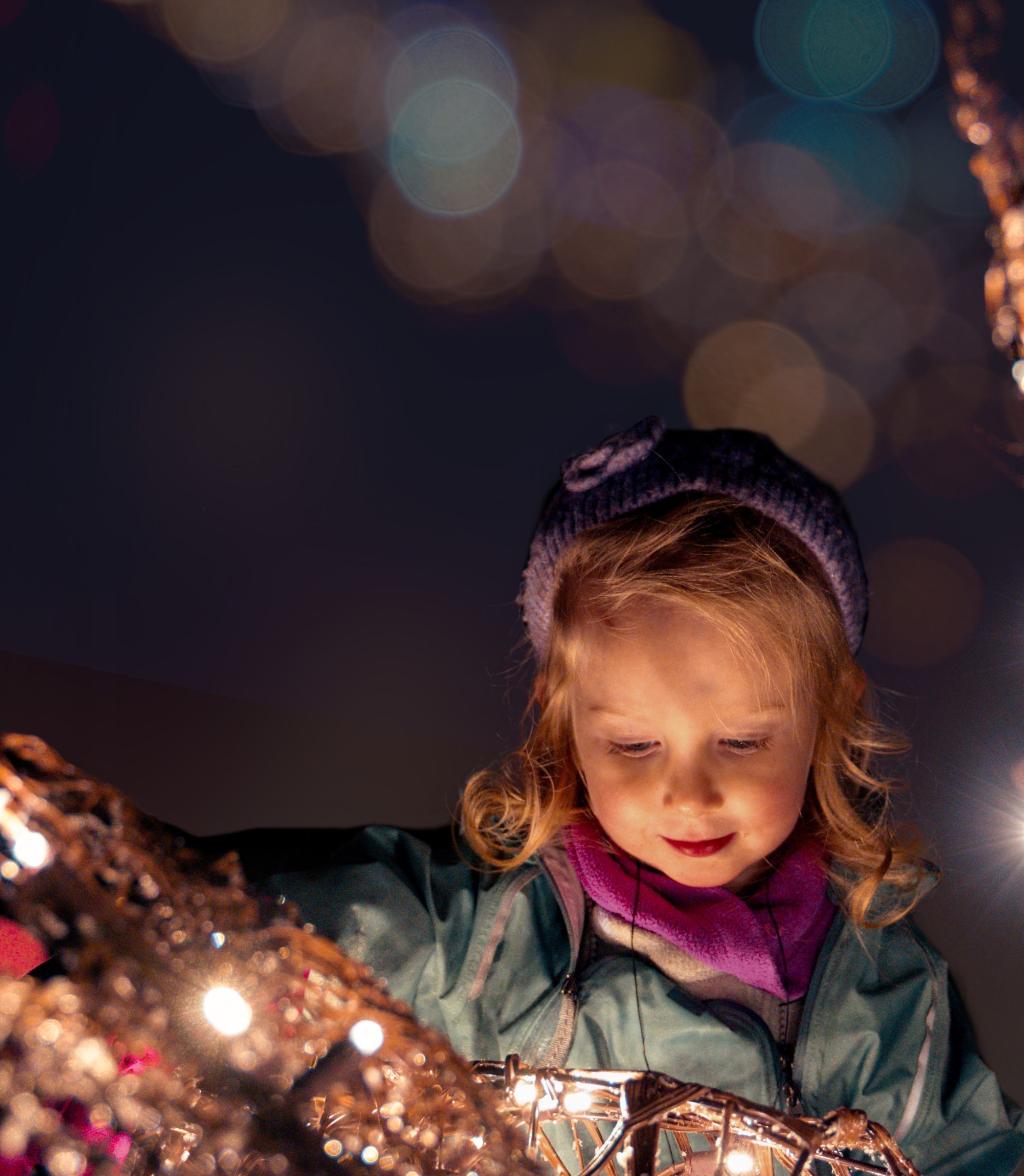 child standing by a winter wonders light decoration, their face is lit up by the glow of the lights