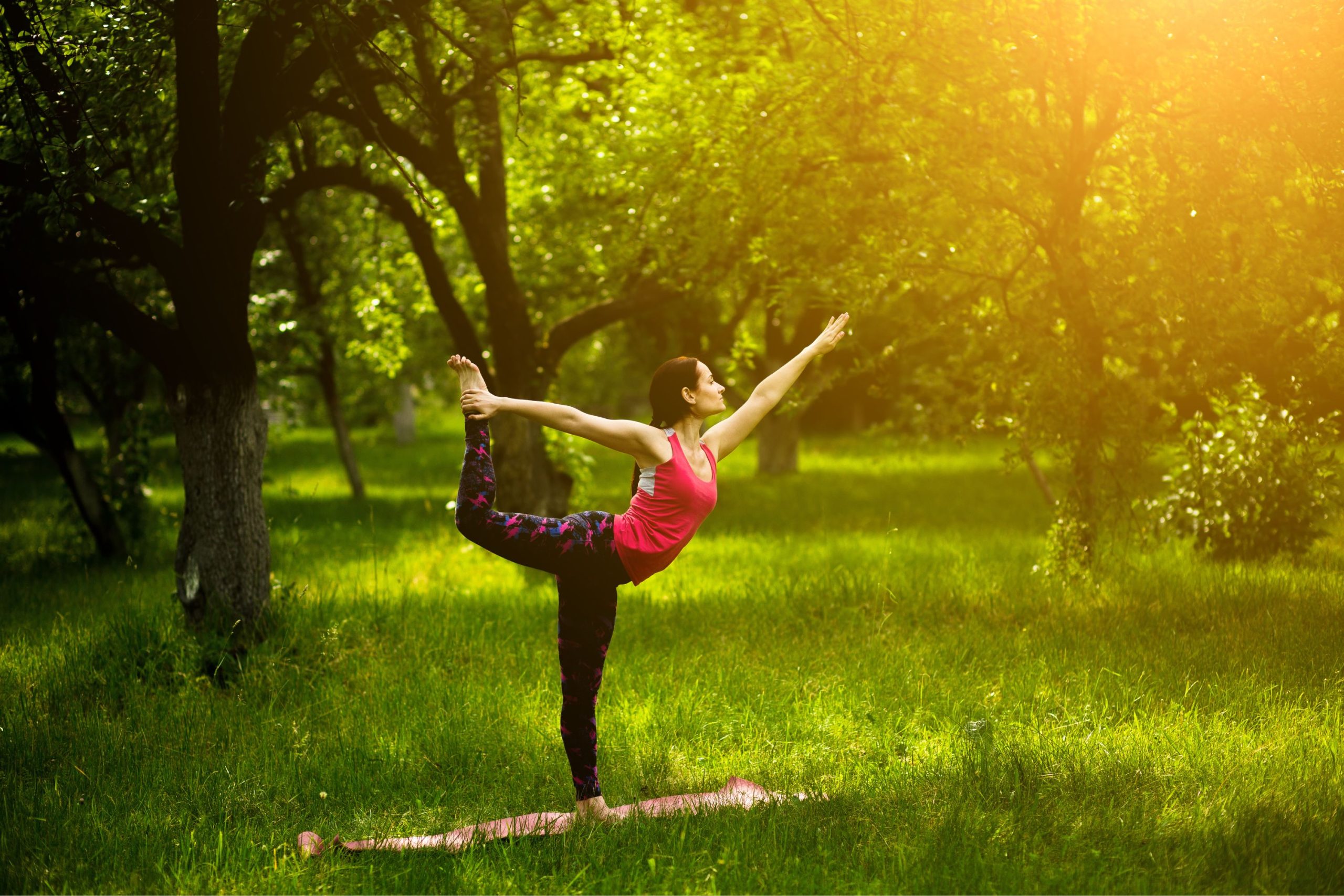 Woman performing yoga on a mat in a grassy and treed area in the summer 